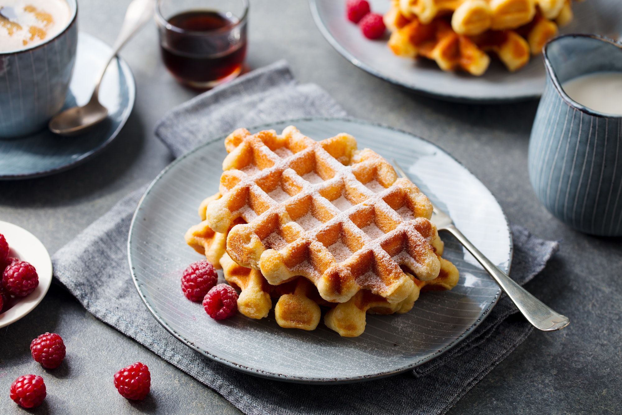 Breakfast Belgian waffles with maple syrup and fresh raspberry. Grey background.
