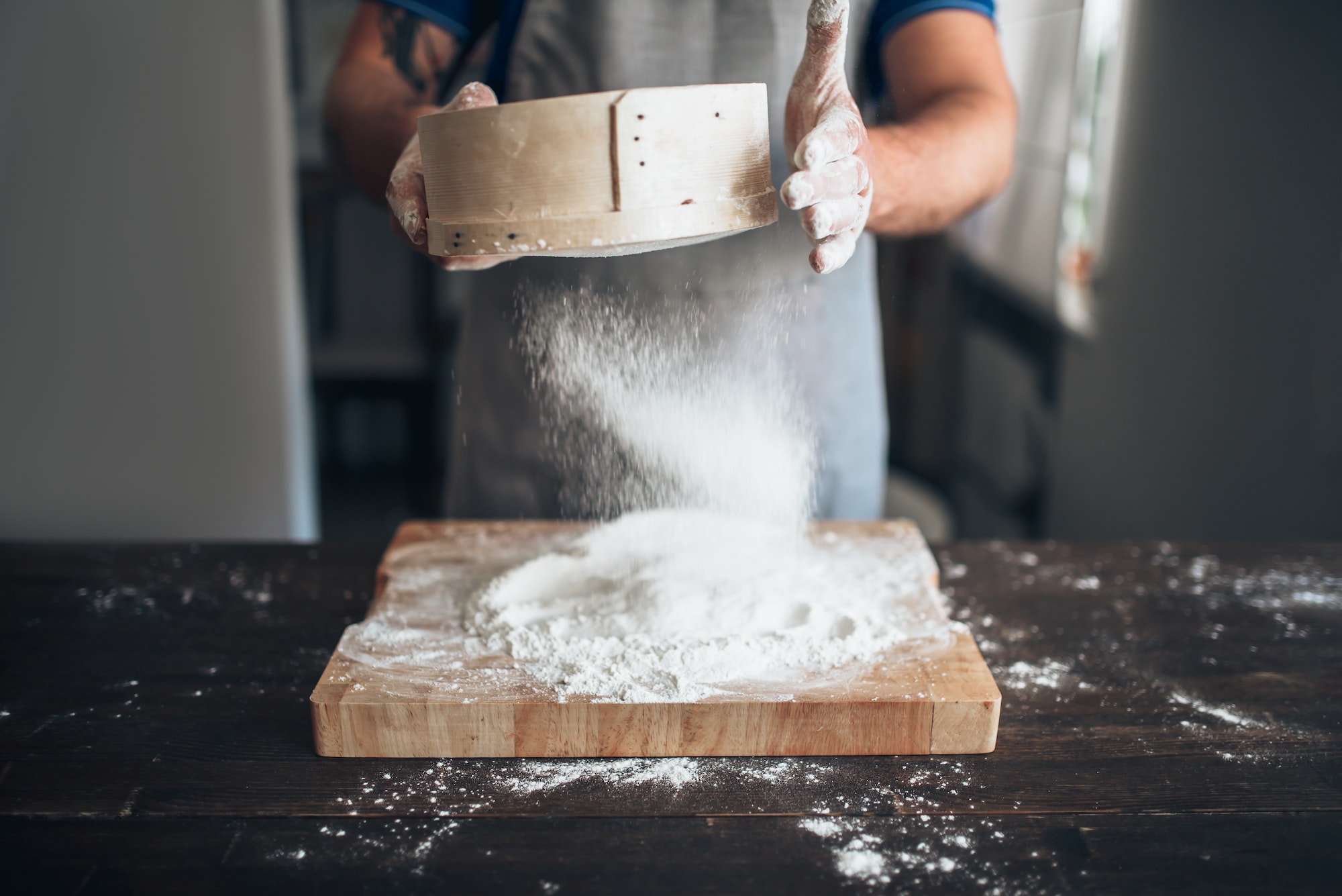 Manos masculinas de panadero filtran la harina a través de un tamiz