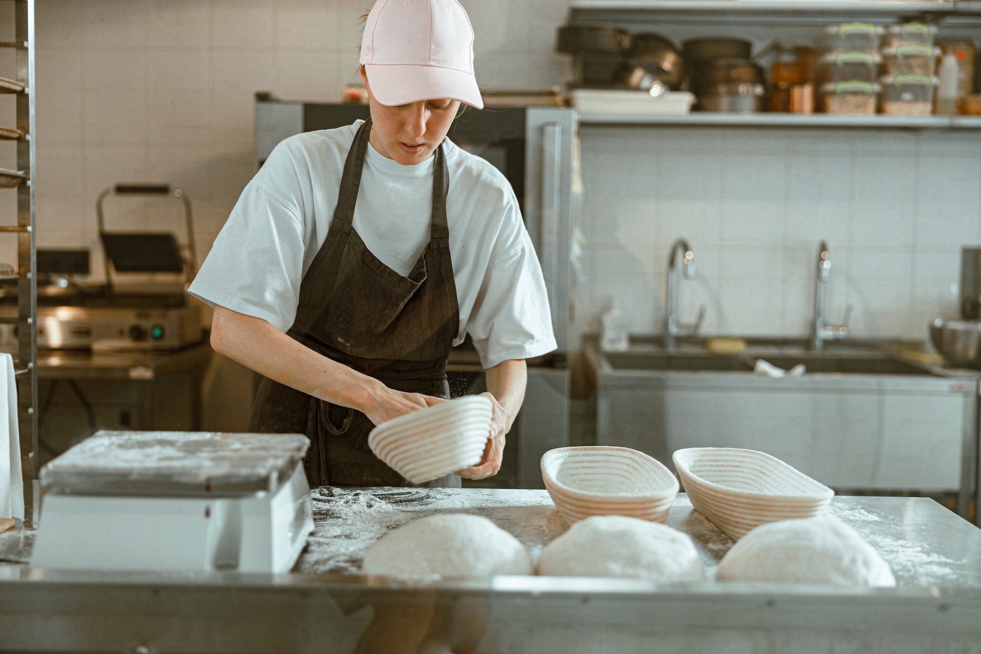 Mujer seria esparce harina dentro de un plato en un obrador de panadería contemporánea